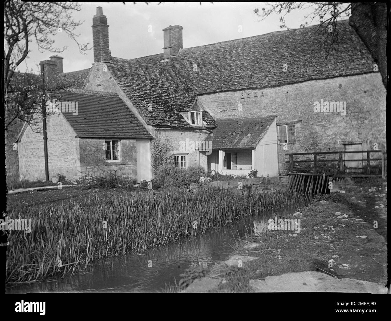 Mill Cottage, Swinbrook, Swinbrook und Widford, West Oxfordshire, Oxfordshire, 1924. Blick nach Nordosten über den Fluss Windrush auf die Rückseite von Mill Cottage. Stockfoto