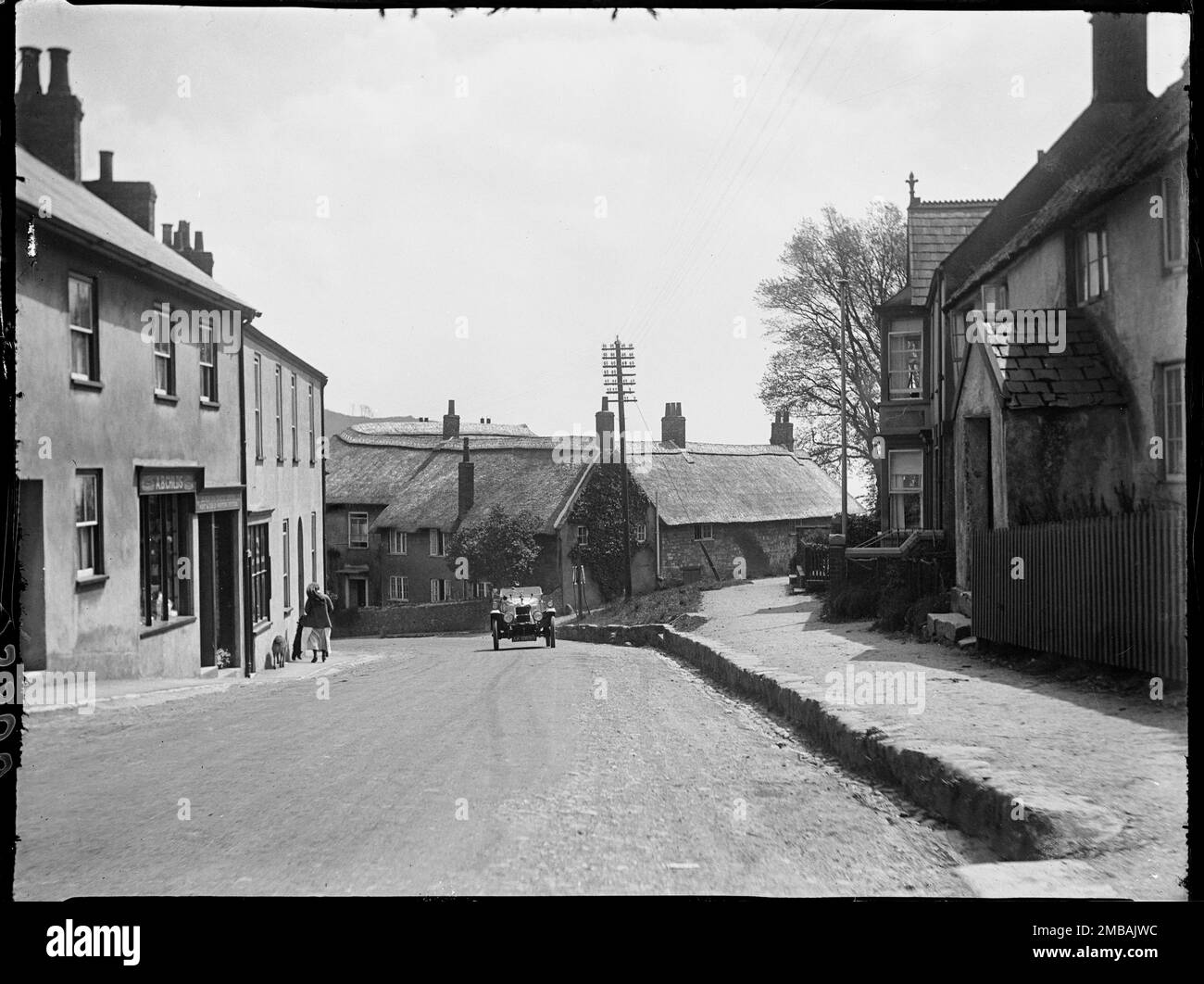 Die Straße, Charmouth, West Dorset, Dorset, 1925. Ein Blick auf die Straße vom Axminster Road End, Blick auf strohgedeckte Hütten an der Kreuzung mit Higher Sea Lane und ein Auto, das den Hügel hinauffährt. Stockfoto