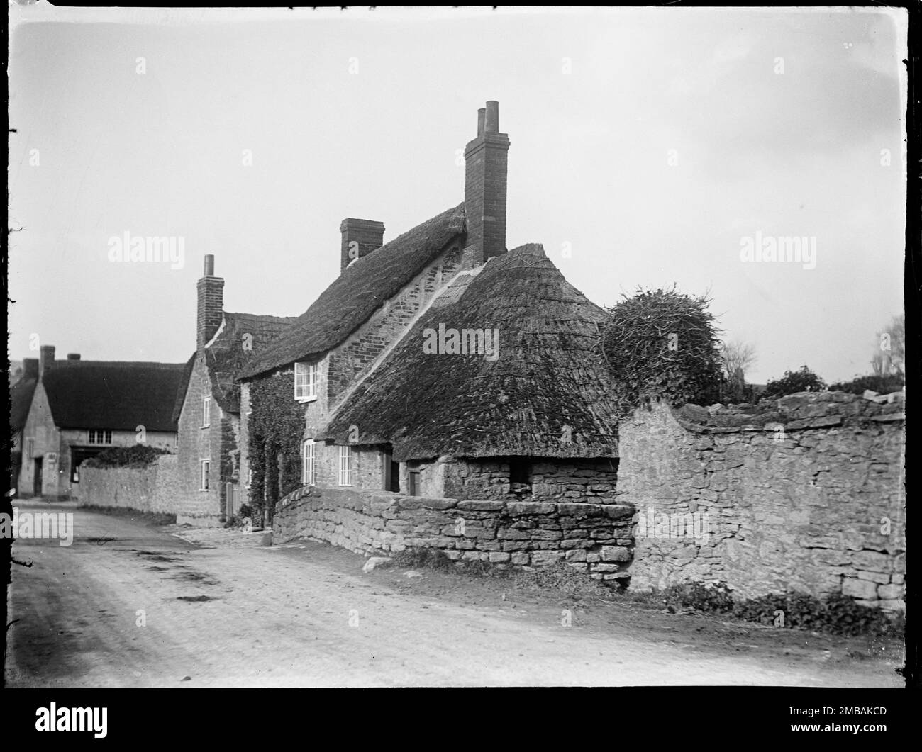 High Street, Burton Bradstock, West Dorset, Dorset, 1922. Eine strohgedeckte Hütte an der High Street in Burton Bradstock mit einem strohgedeckten Nebengebäude, das an das Haus angeschlossen ist. Auf einer Anhöhe auf der Straße neben einem Geschäft, mit einer Hütte, die später abgerissen wurde, aber sich auf der Nordseite eines Flusses befand, der unter der Straße fließt. Stockfoto