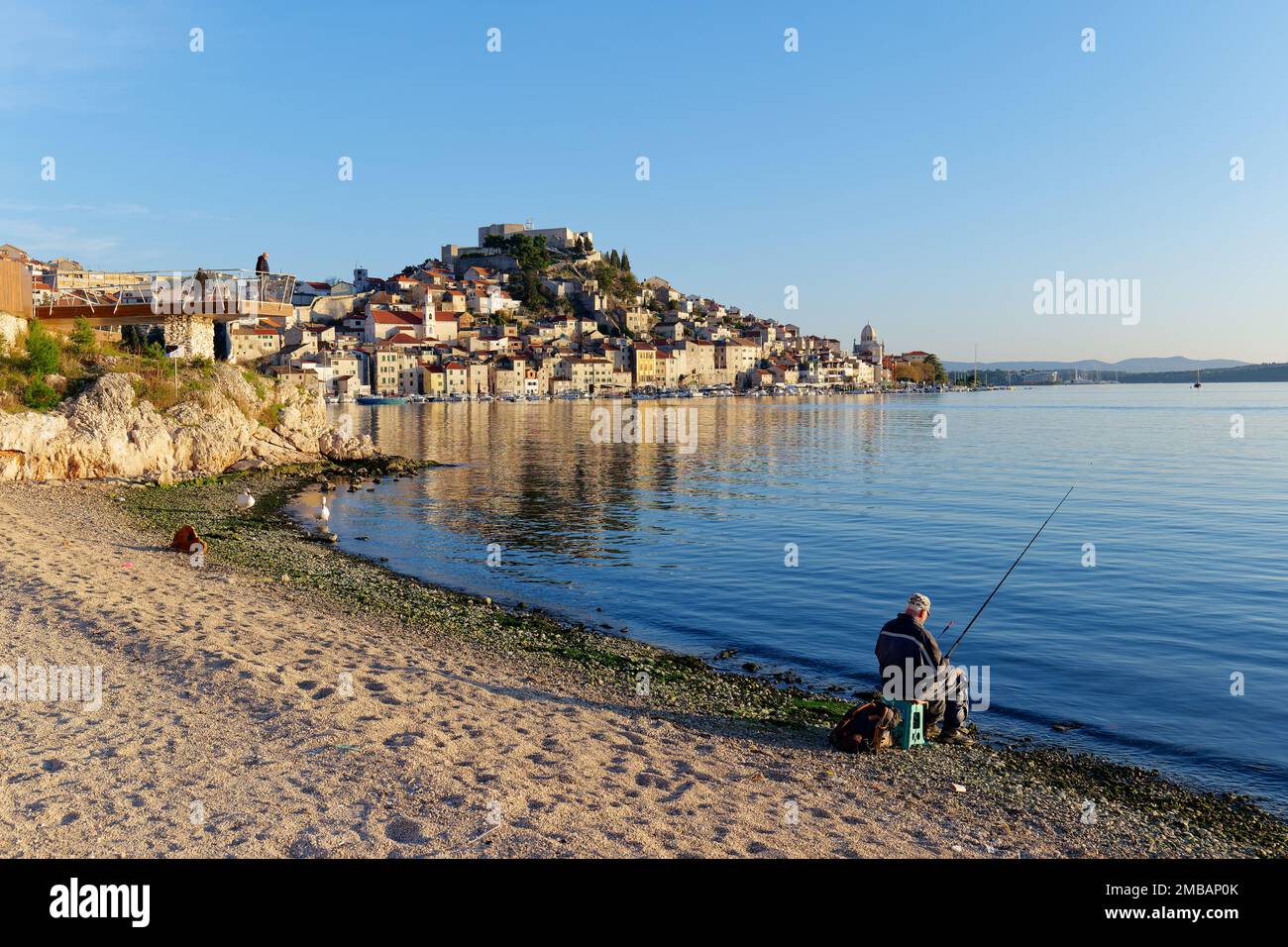 Fischer, die in der Adria neben der Stadt Sibenik in Kroatien angeln, während die wunderschönen Farben des Sonnenuntergangs zu sehen sind. Urlaub und Urlaub an der Küste. Stockfoto