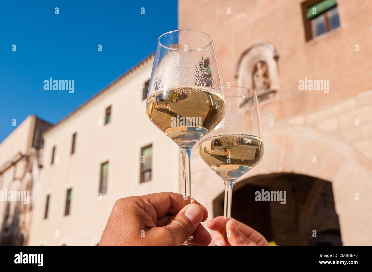 Zwei Hände halten ein Glas Weißwein vor dem Eingang zum Monestir de Poblet. Monestir de Poblet, Katalonien, Spanien Stockfoto