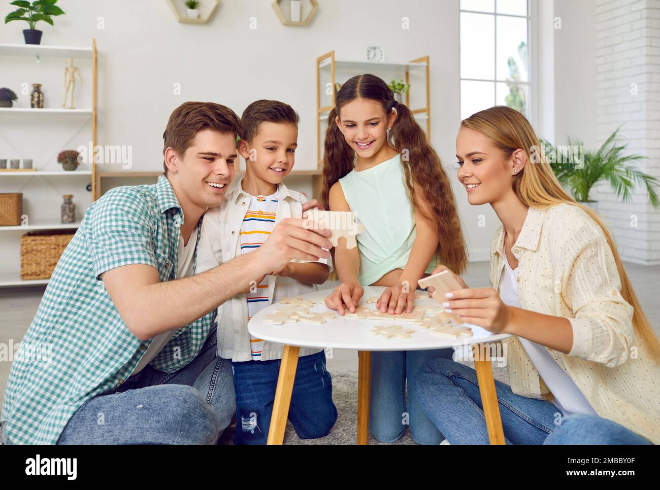 Glückliche Familie mit zwei Kindern spielt am Wochenende am Tisch, der zu Hause auf dem Boden sitzt. Stockfoto