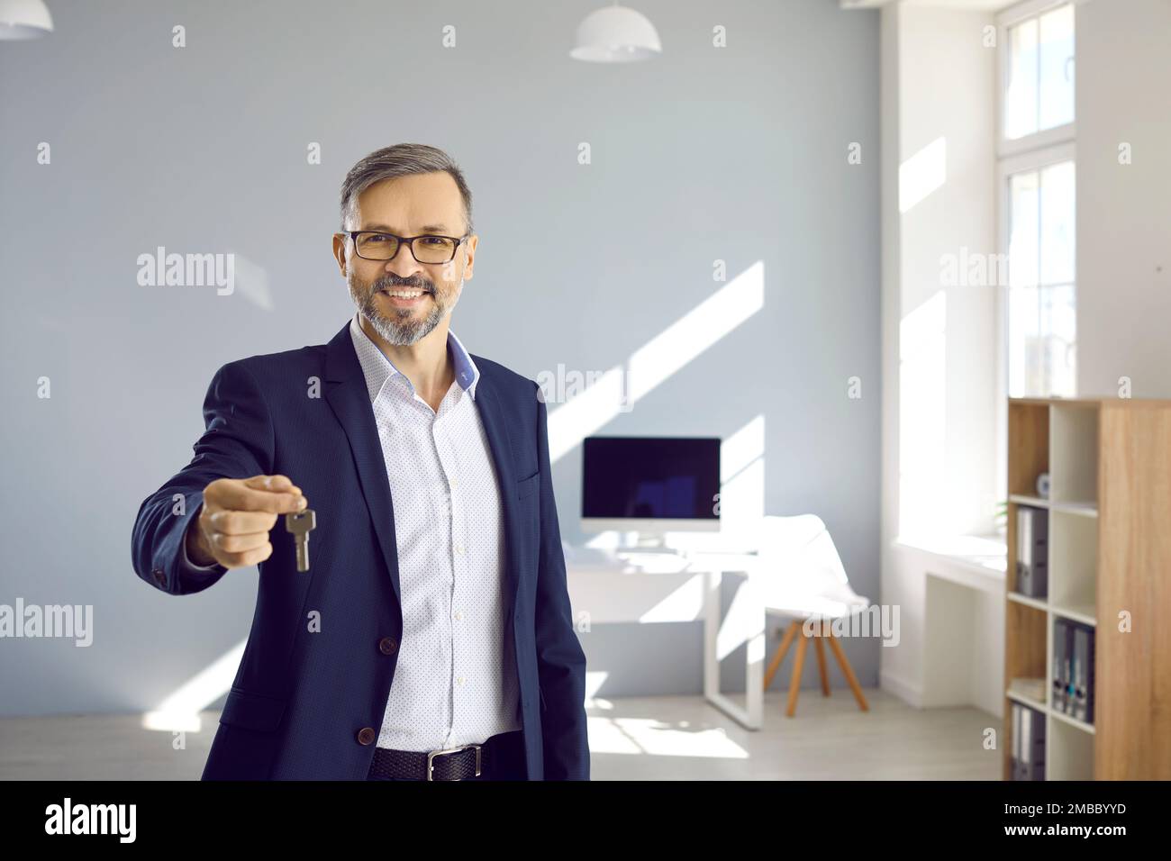Porträt eines freundlichen männlichen maklers, der die Schlüssel zu Haus oder Büro zeigt, das er verkauft oder geleast hat. Stockfoto