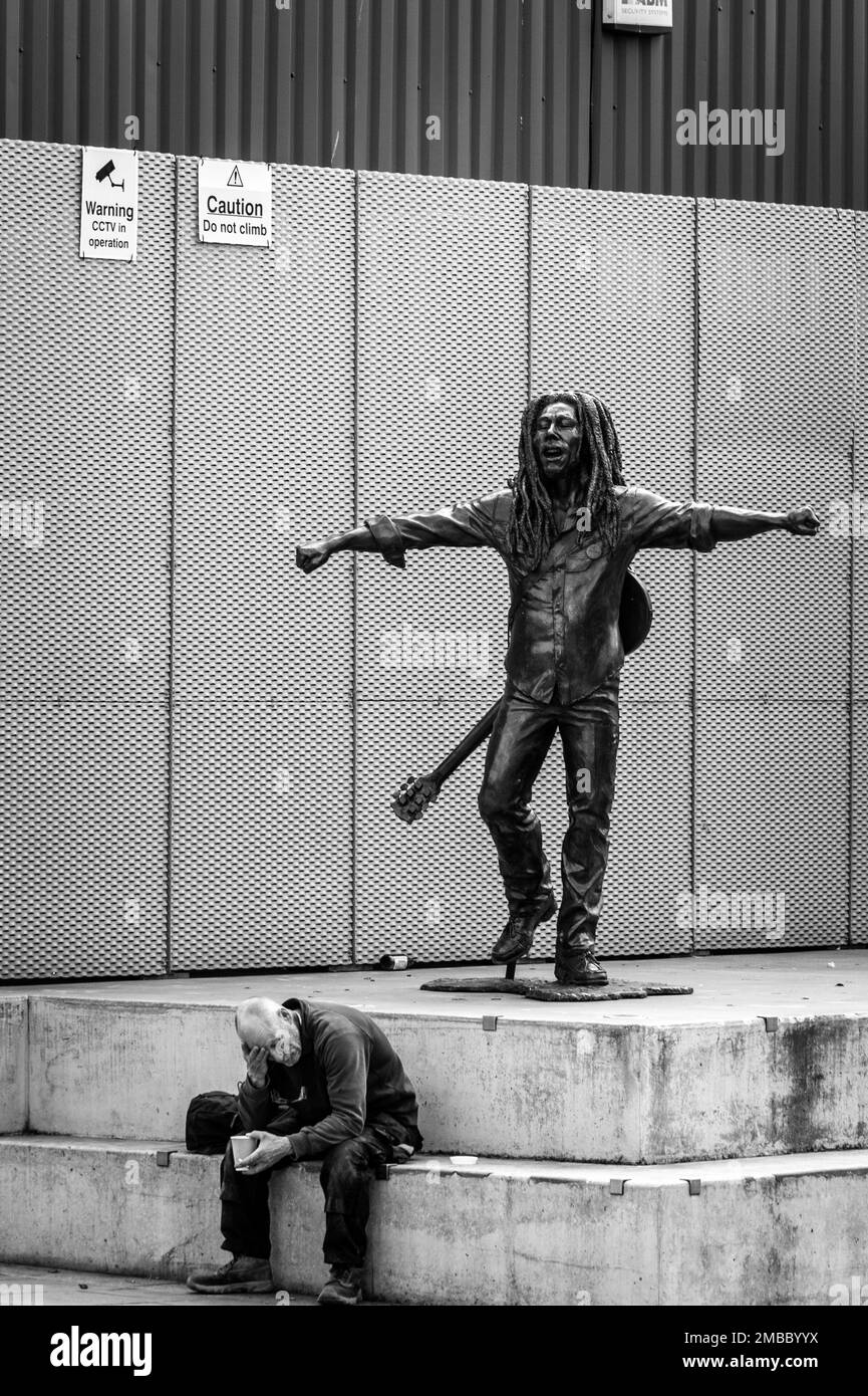Ein Obdachloser sitzt unter einer Bob-Marley-Statue Stockfoto