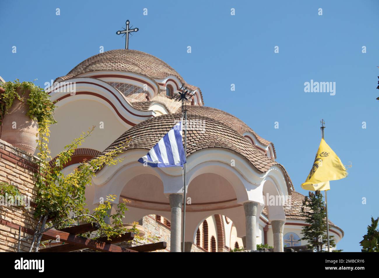 Blick auf den Hinterhof des Klosters des Erzengels Michael in Griechenland, Thasos Island, mit leuchtend orangefarbenen Wänden und Dach und riesigen Kirchenglocken Stockfoto