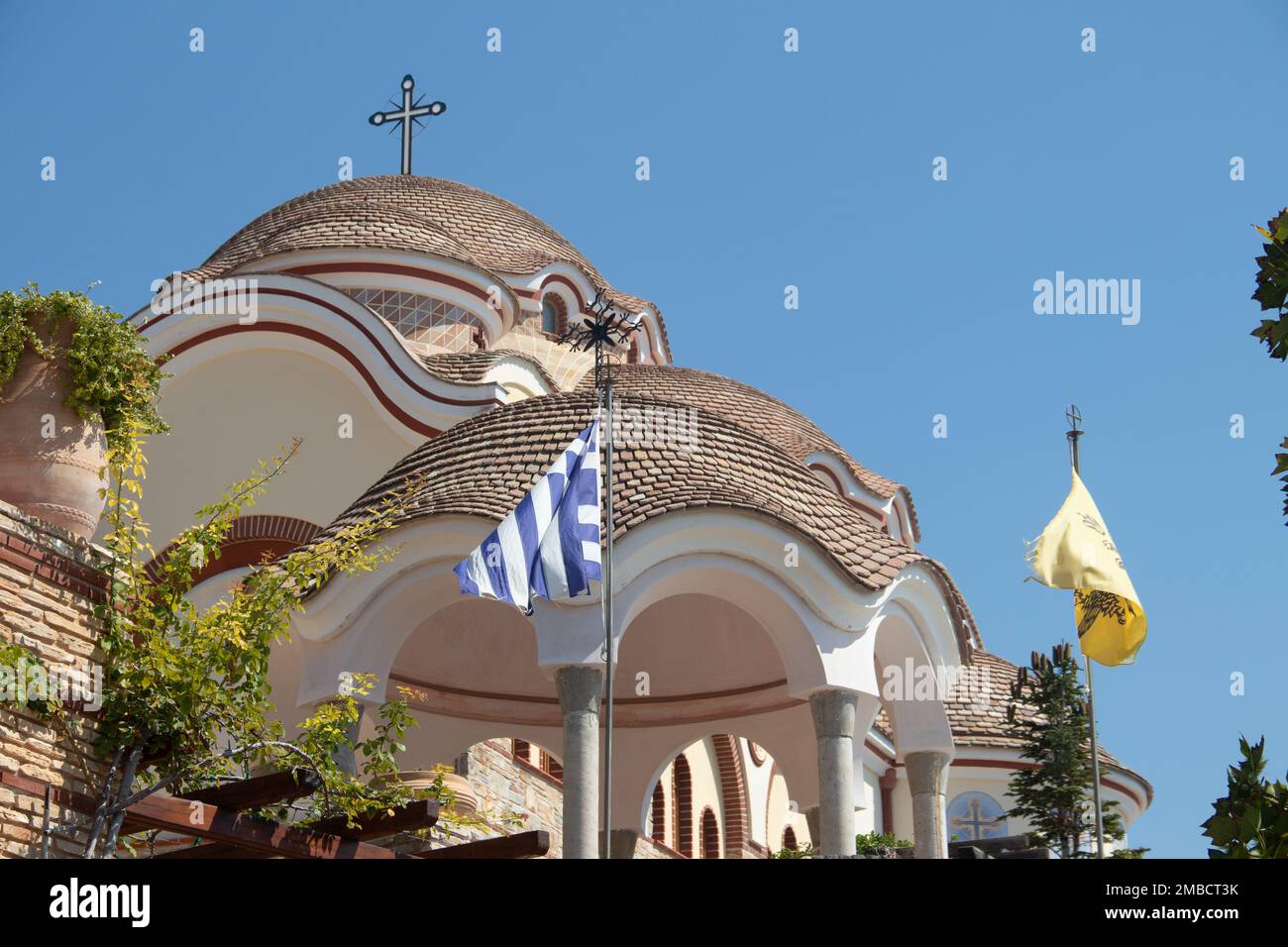 Blick auf den Hinterhof des Klosters des Erzengels Michael in Griechenland, Thasos Island, mit leuchtend orangefarbenen Wänden und Dach und riesigen Kirchenglocken Stockfoto
