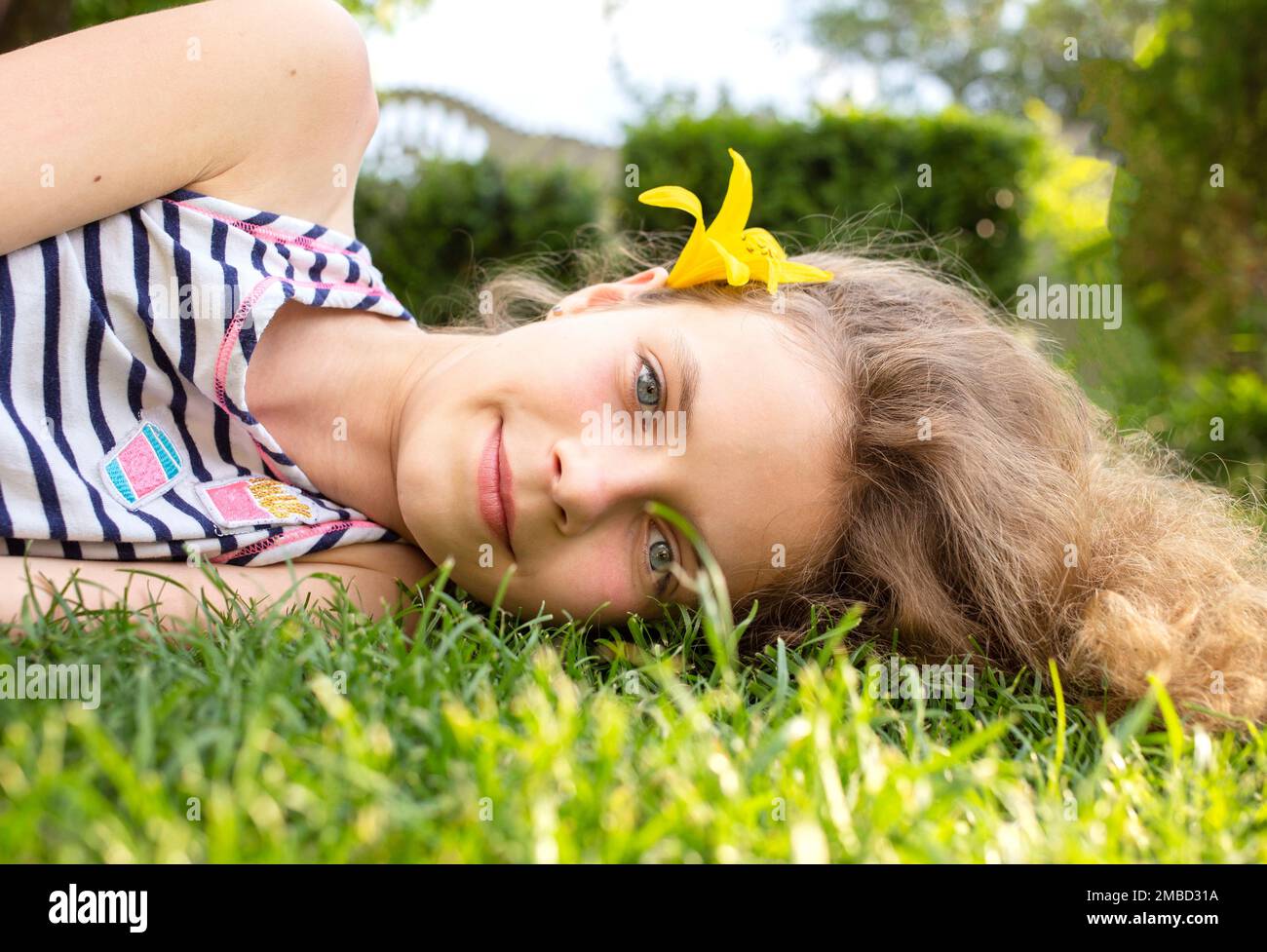 Gesichtsbild eines lächelnden, 12-jährigen Mädchens, das an sonnigen Tagen auf Gras liegt. Naturgenuss im Freien, Entspannung, Träume. Hallo Sommer, Spri Stockfoto
