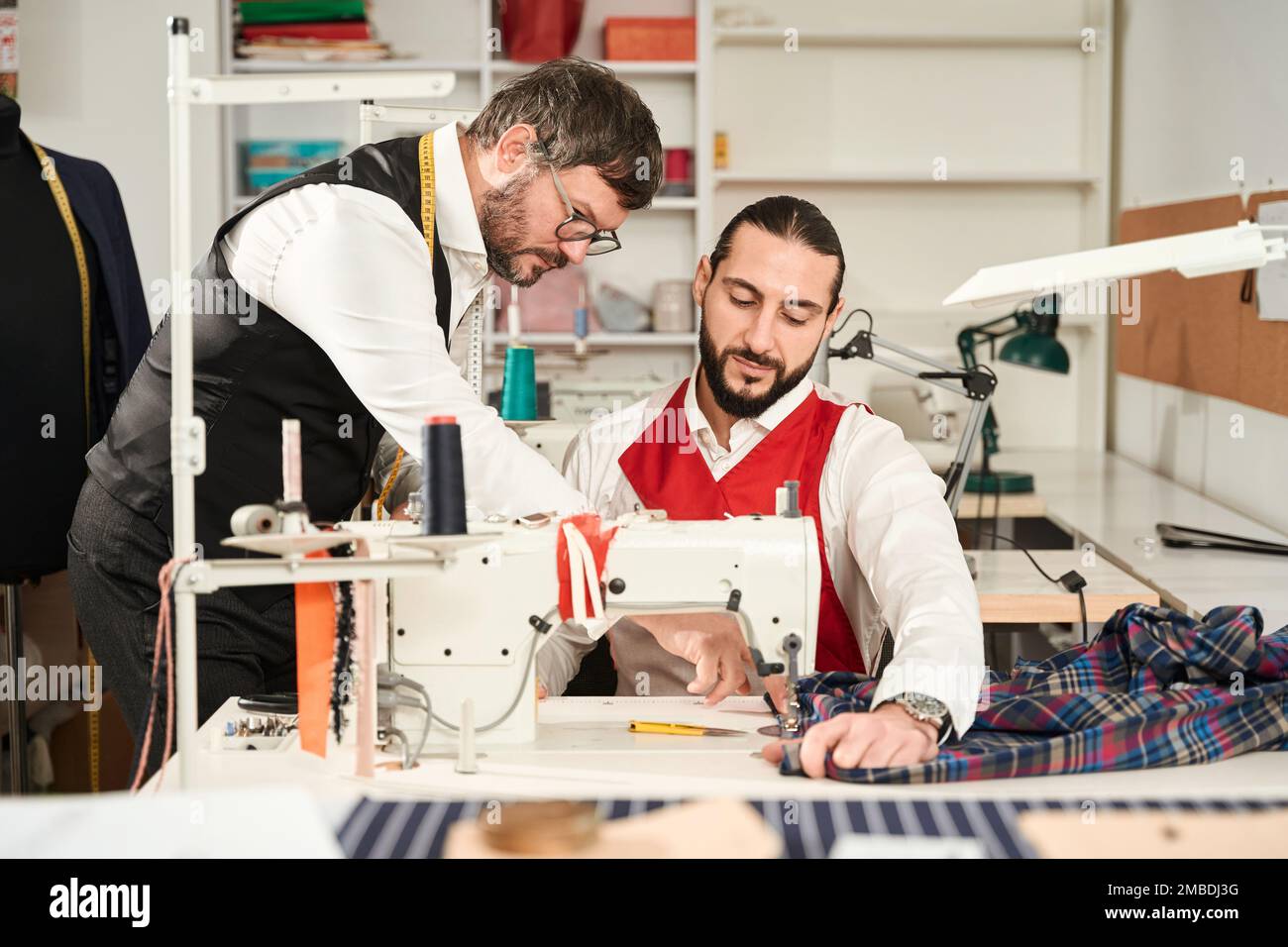 Auszubildender, der an Overlocker arbeitet, unter Aufsicht eines Experten Stockfoto