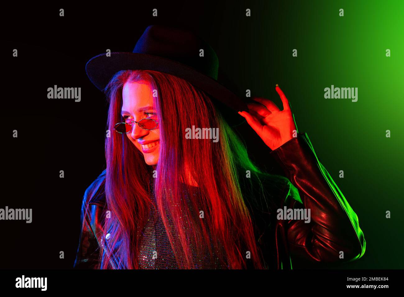 Modische Frau in mehrfarbigem Neonlicht. Rauchiger Hintergrund, Nachtparty, Disco-Club. Z-Generation rätselhafte schöne Dame in Lederjacke, Hut Stockfoto