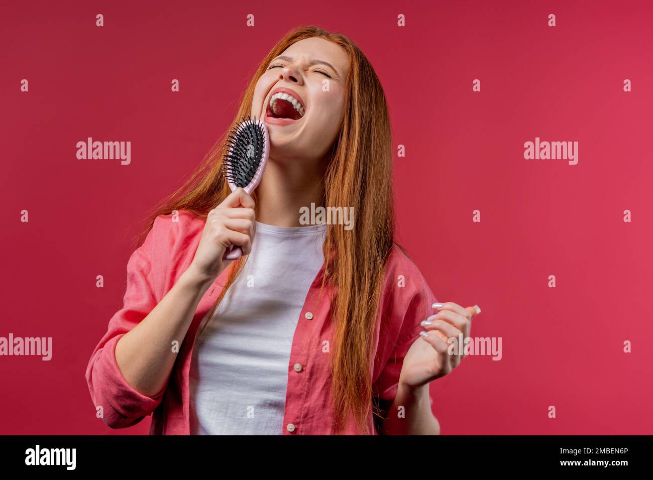 Frau singt, tanzt mit Haarbürste statt Mikrofon auf pinkfarbenem Hintergrund. Lady hat Spaß, hört Musik, Karaoke, träumt davon, berühmt zu werden. Stockfoto