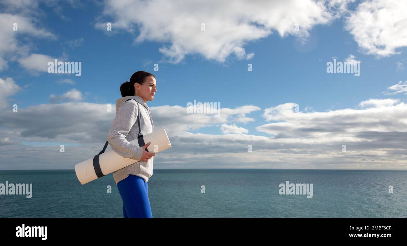 Fit Frau mit Yoga-Matte, die sich auf das Training am Meer vorbereitet. Stockfoto