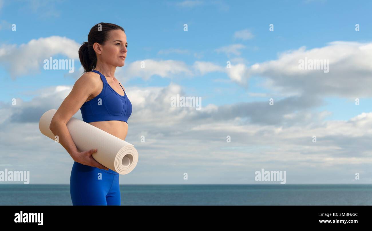 Fit Frau mit Yoga-Matte, die sich auf das Training am Meer vorbereitet. Stockfoto