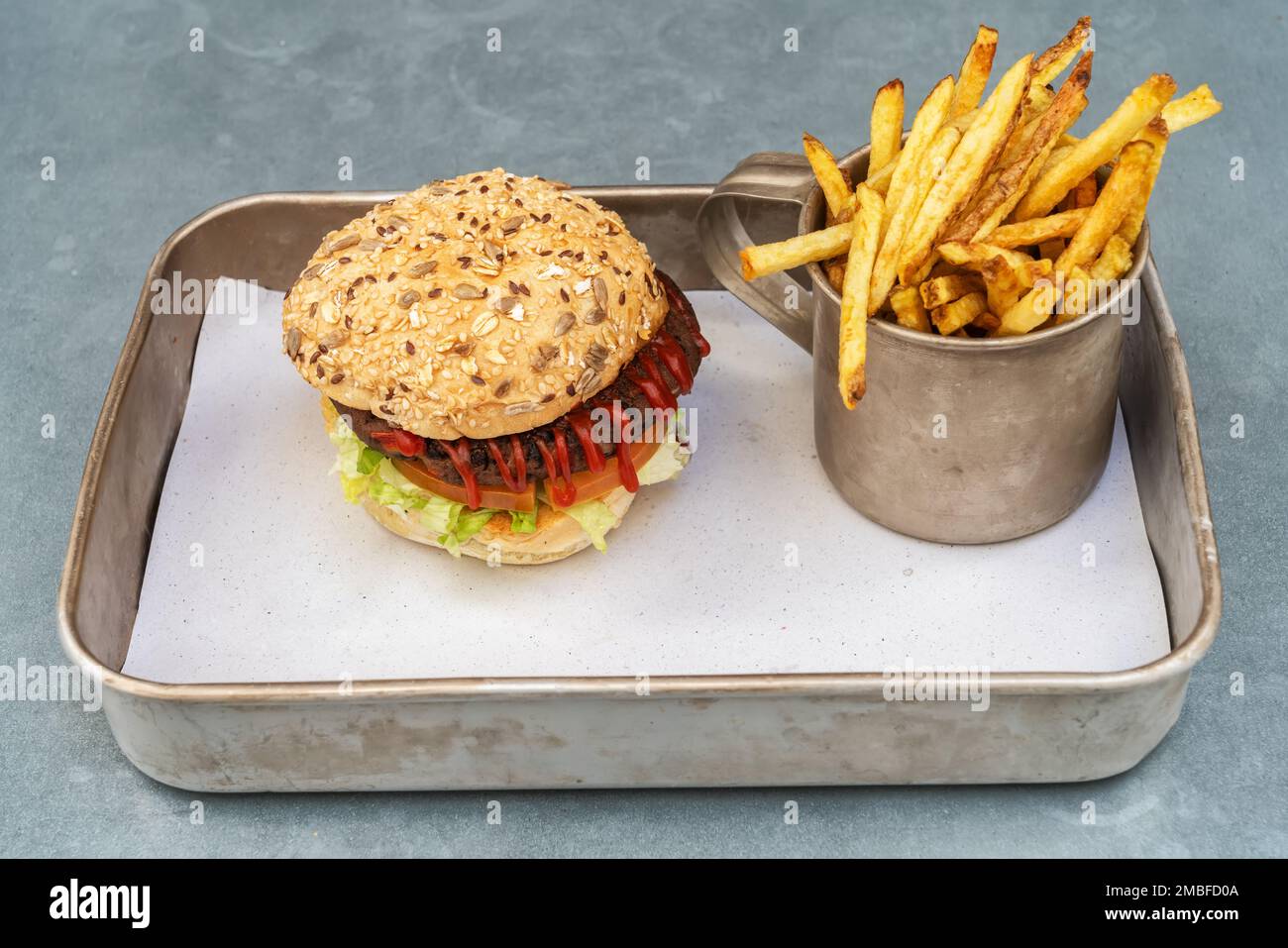 Vegetarischer Hamburger aus Bohnen, Gemüse und Ketchup-Brötchen und gebratenen Kartoffeln in einer alten Tasse auf einem Metalltablett. Stockfoto