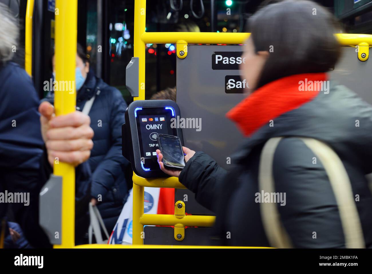 Eine Person bedient ein Smartphone mit einem OMNY kontaktlosen Zahlungsleser in einem NYC Transit Bus. Das Lesegerät akzeptiert EMV-Zahlungen über NFC Stockfoto