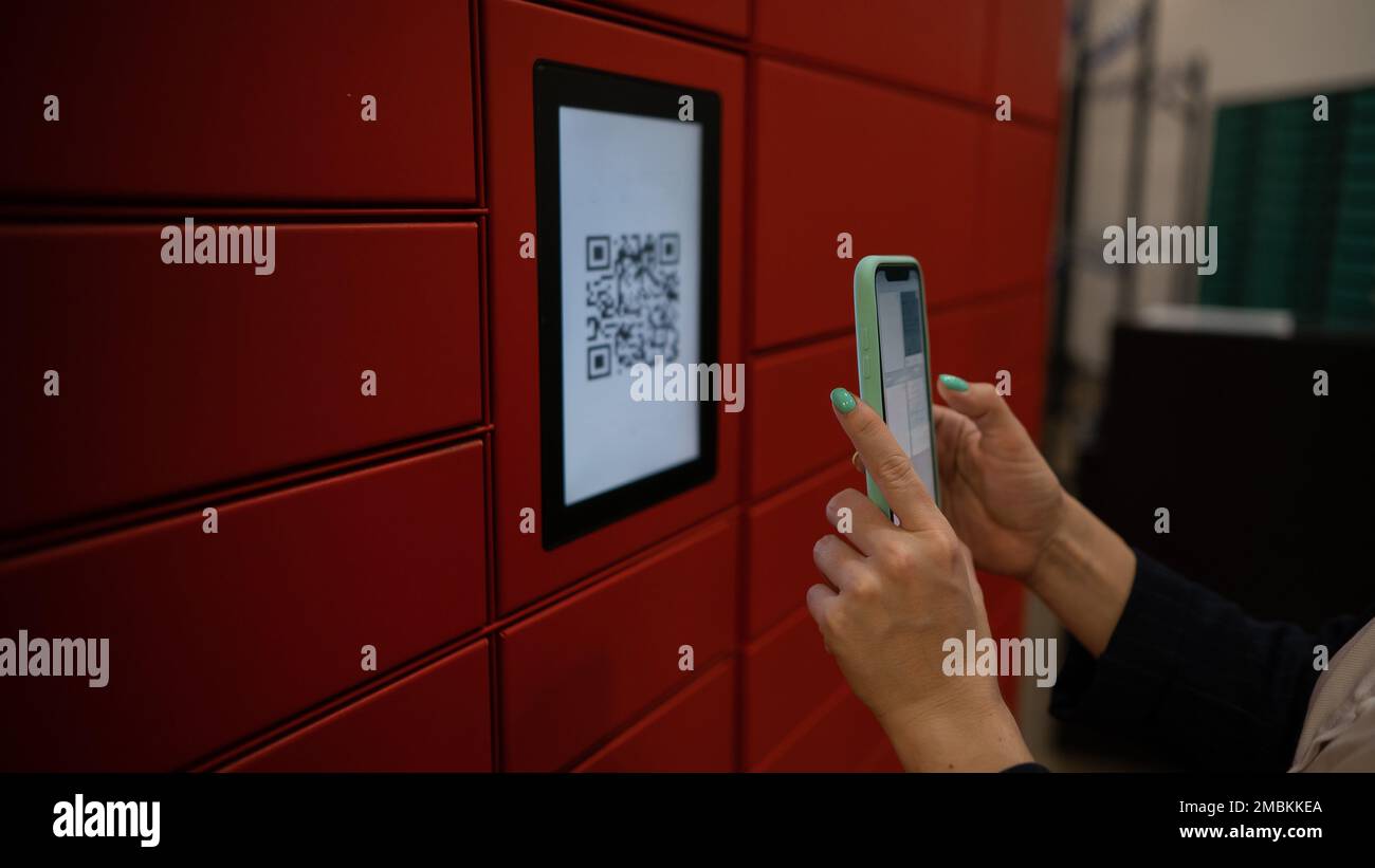 Eine Frau scannt einen roten Code, um ein Paket an einer Paketmaschine abzuholen. Automatisierte Postfächer. Stockfoto