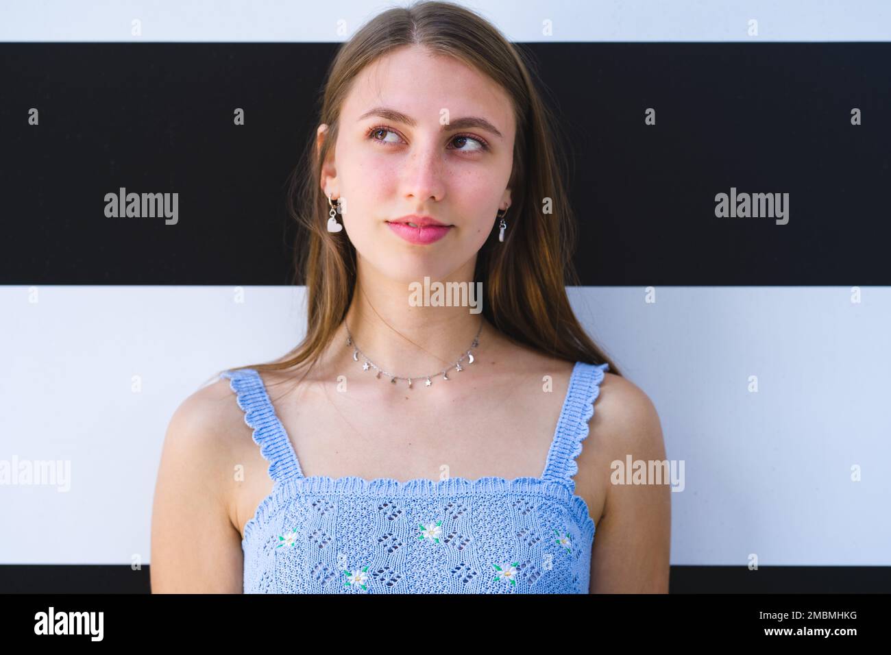 Nahaufnahme des lächelnden Teenage Girl, das vor der schwarz-weiß gestreiften Wand steht und nach oben und nach rechts schaut Stockfoto