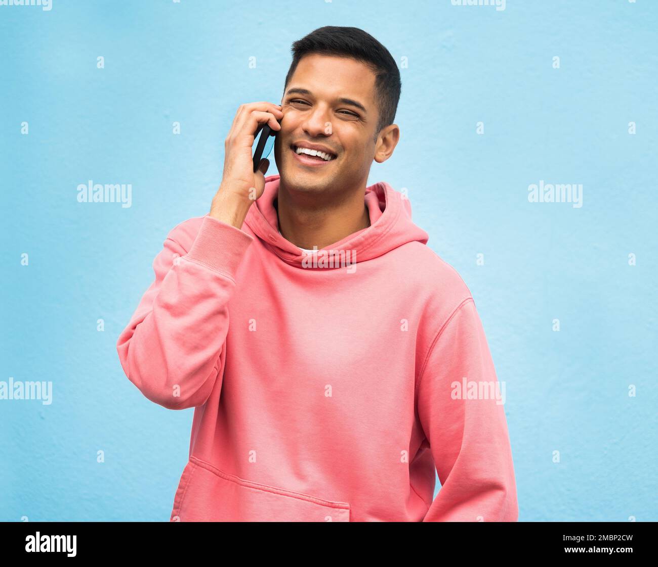 Gelegenheitsmann, Anruf und Lächeln für die Kommunikation, isoliert auf blauem Hintergrund. Glücklicher Mann, Person oder Jungs mit rosa Jacke in der Diskussion Stockfoto