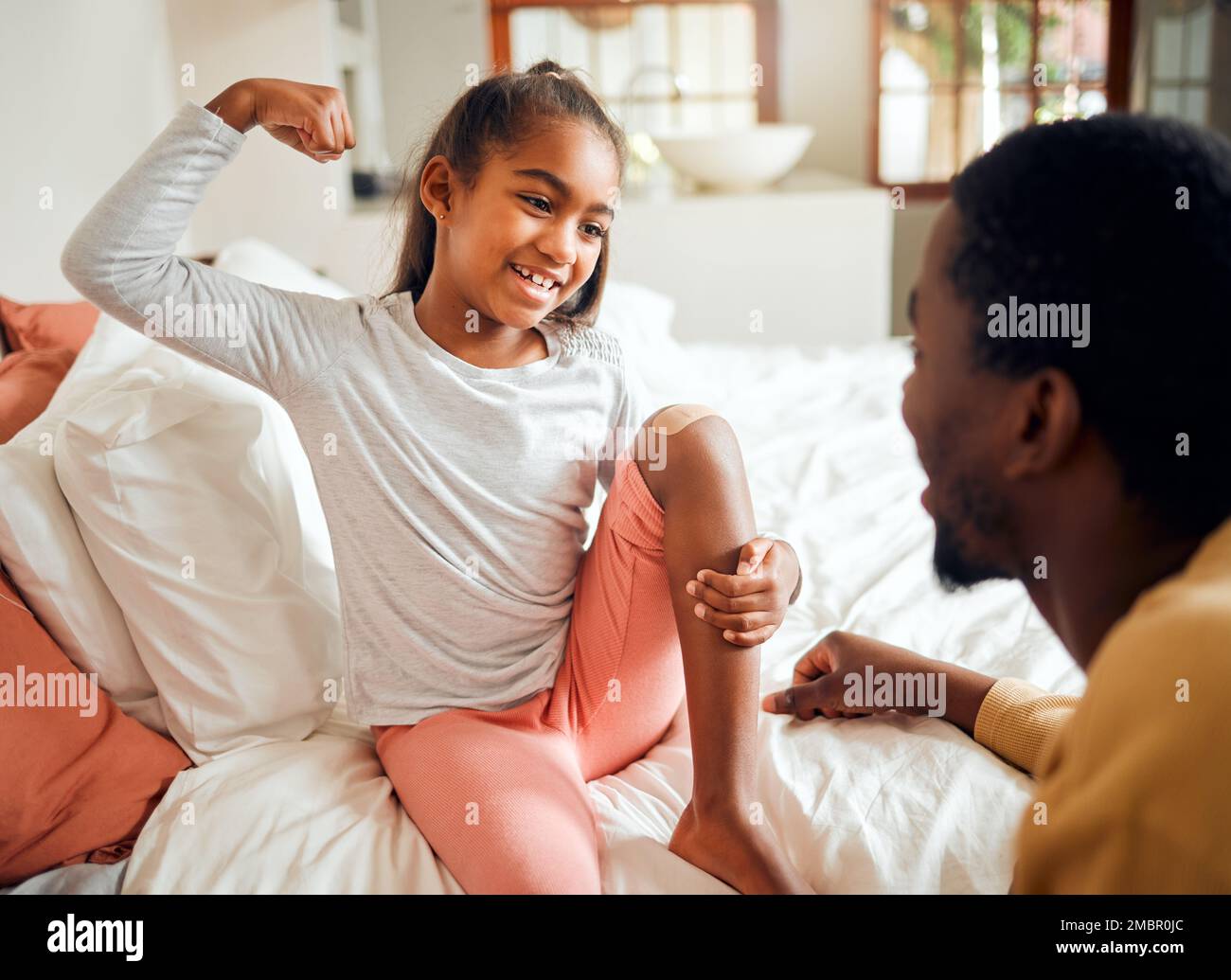 Familie, Bett und Vater mit Mädchen und Bandhilfe zeigen Muskeln, mutige und starke Geste für Verletzungen. Liebe, Heim und glücklicher Vater, der dem Kind mit dem Gips hilft Stockfoto