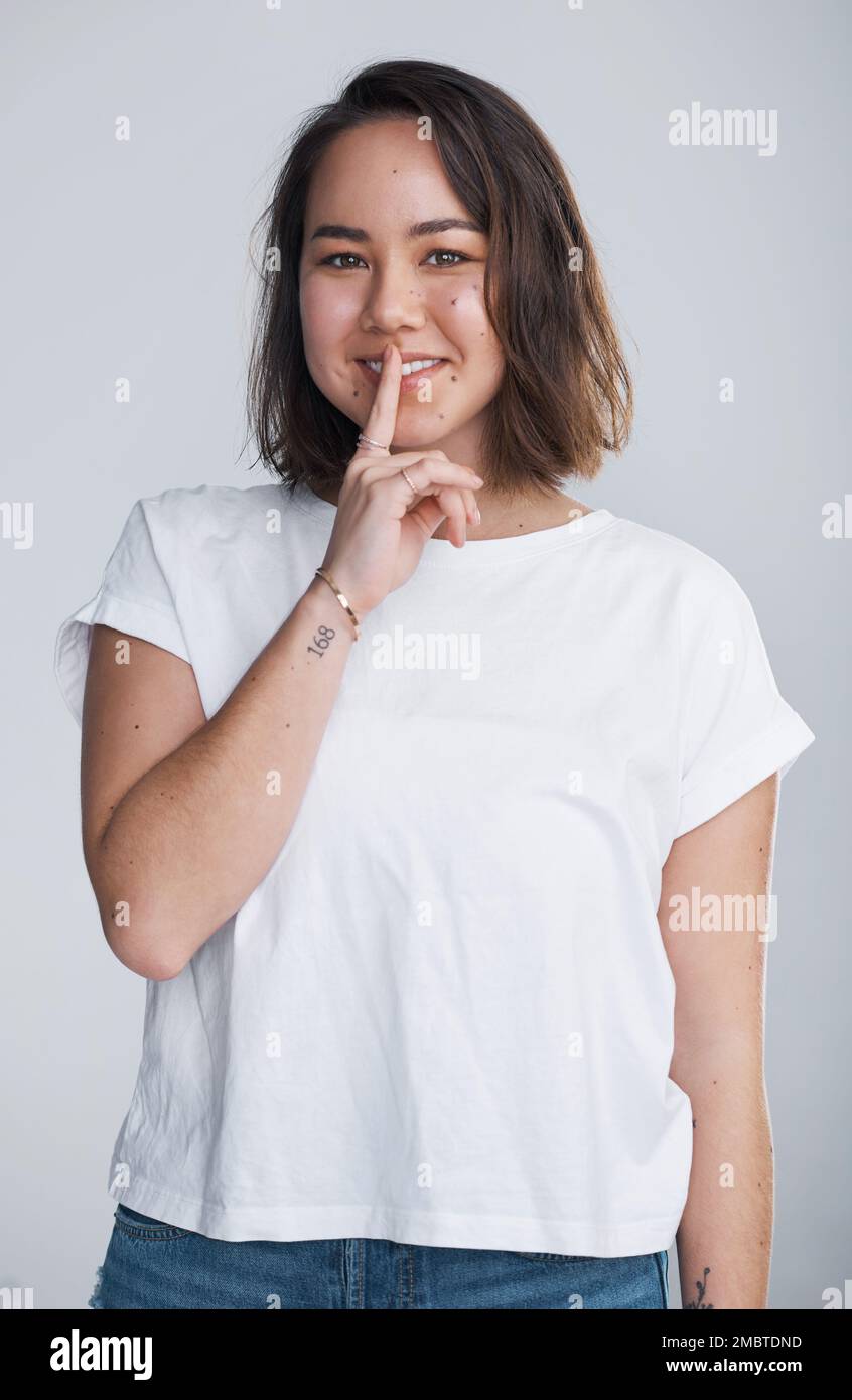 Ich hoffe, du kannst ein Geheimnis bewahren. Eine schöne junge Frau, die mit den Fingern auf den Lippen posiert. Stockfoto