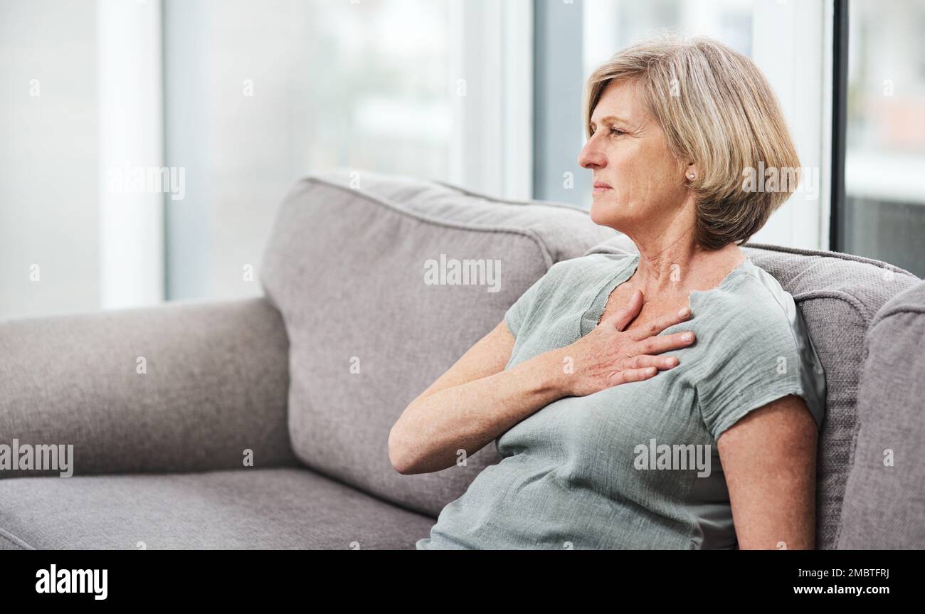 Brustschmerzen sind besorgniserregend. Eine ältere Frau, die Schmerzen in der Brust hat, während sie zu Hause auf dem Sofa sitzt. Stockfoto