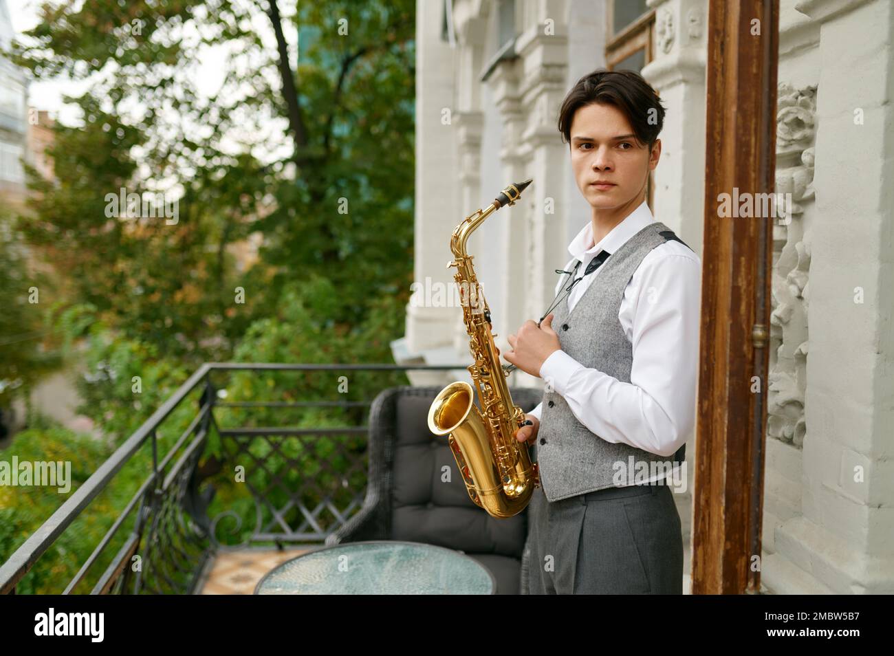 Junger Mann mit Saxofon auf der Balkonterrasse Stockfoto