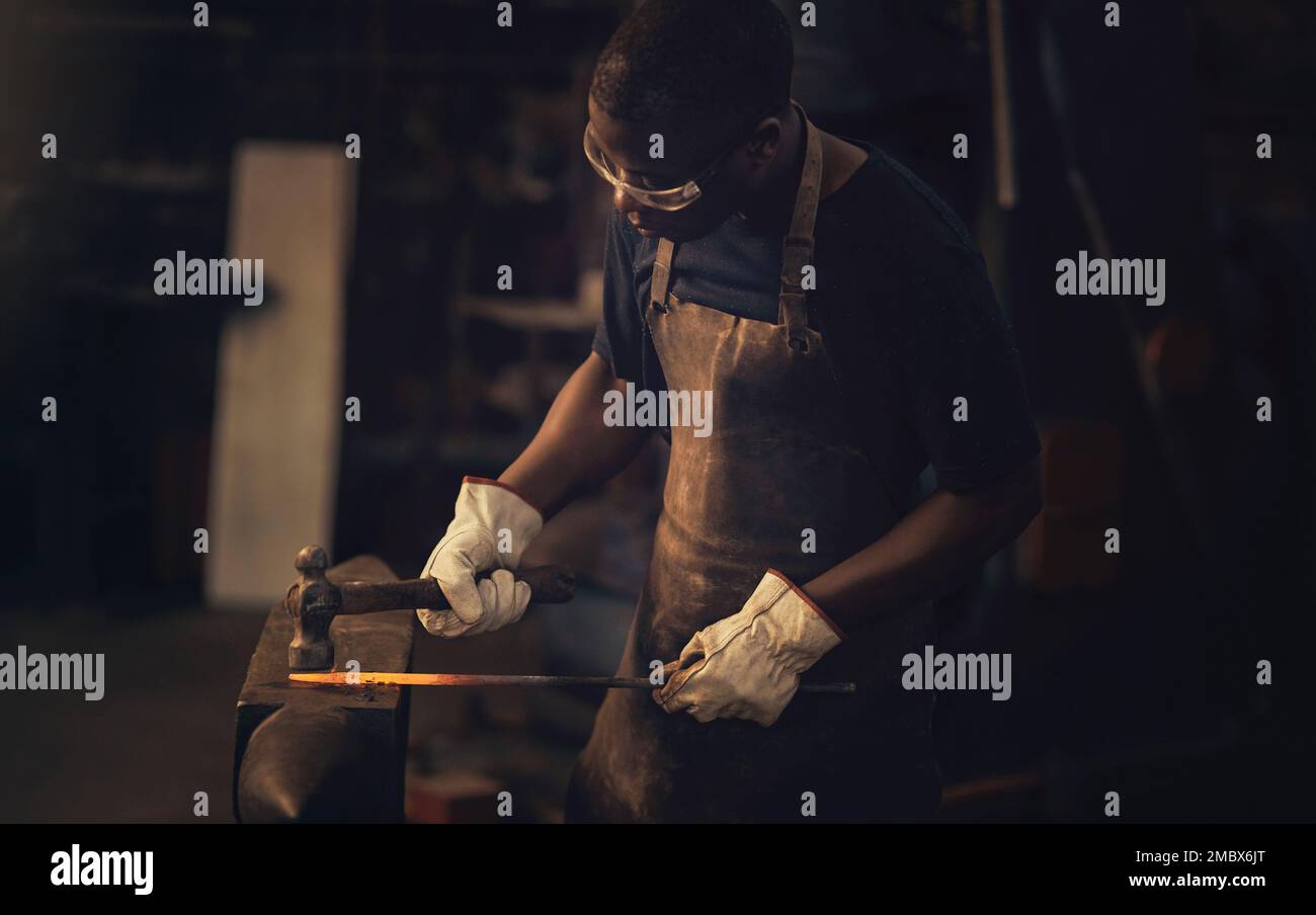 Vorschlaghämmer, das Original-Elektrowerkzeug. Ein junger Mann, der einen heißen Metallstab mit einem Hammer in einer Gießerei schlägt. Stockfoto