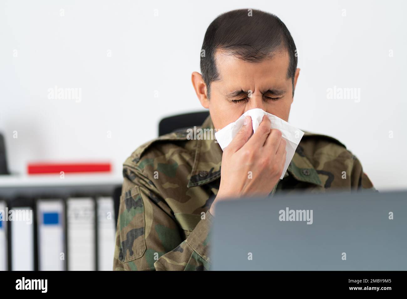 Aufnahme eines erwachsenen Soldaten, der sich bei der Arbeit mit einem Taschentuch die Nase bläst Stockfoto