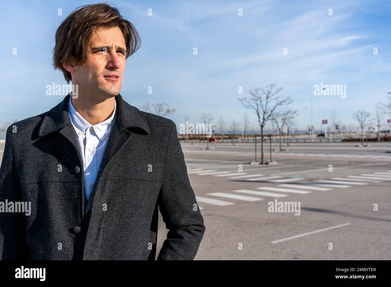 Aufmerksamer erwachsener Geschäftsmann in stilvollem Mantel, der auf der Straße steht und pensiv wegschaut, während er über ein neues Startup-Projekt nachdenkt Stockfoto