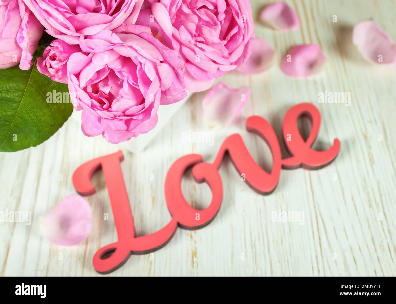 Rosa Rosen und Blütenblätter auf weißem Holzschreibtisch und rotes Holzwort Liebe. Hintergrund zum valentinstag. Stockfoto