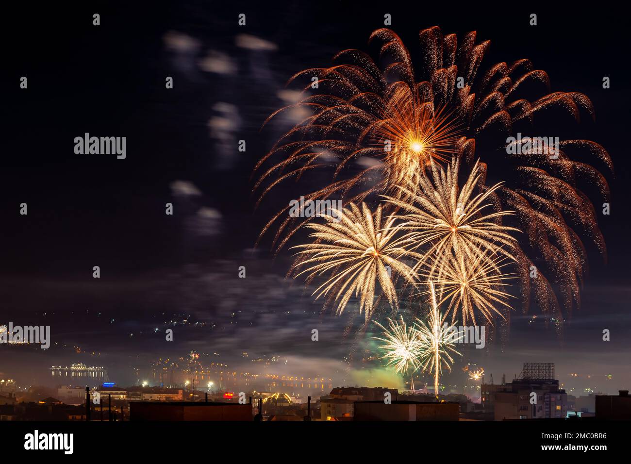 Festliches Feuerwerk am Nachthimmel. Gelbes orangefarbenes Feuerwerk, Explosionen über der Stadt, um Feiertage zu feiern. Pyrotechnik für das Fest-Konzept. Stockfoto