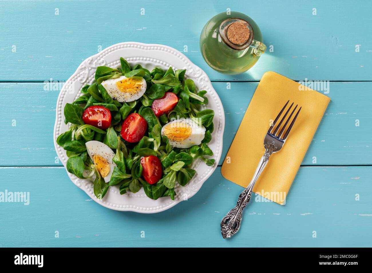Salat aus Lämmern, Salat, Ei und Tomate. Cornsalatblätter, gekochtes Ei und Tomaten auf einem weißen Teller und Gabel über einem türkisfarbenen Holztisch. Stockfoto