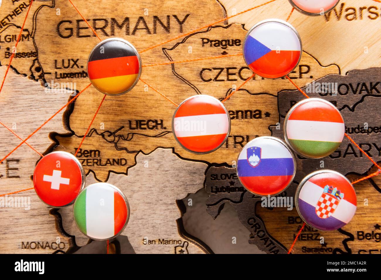 Deutschland, Tschechische Republik, Italien, Slowenien, Ungarn, Schweizer und kroatische Flaggen auf den Nadeln, die mit rotem Faden auf einer Holzkarte verbunden sind. Markierung besuchter Orte. Reiseplanung. Stockfoto