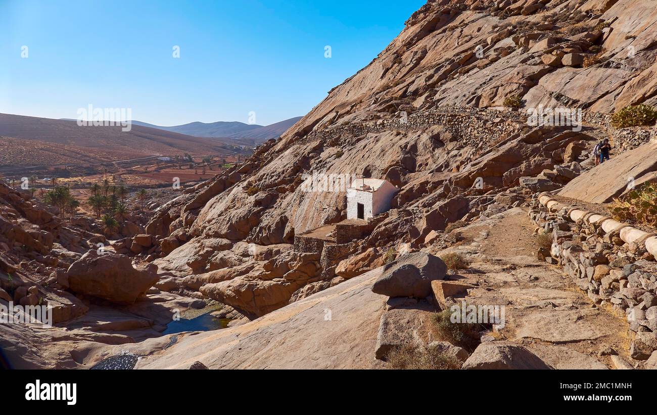 Ermita de La Pena, Felsen, felsiger Wanderweg, weiße kleine Felskapelle, Kapelle, blauer wolkenloser Himmel, Barranco de Las Penitas, Fuerteventura, Kanarienvogel Stockfoto