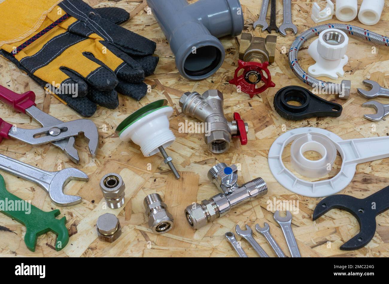 Sanitärwerkzeuge, Teile, Rohrleitungskomponenten und Handschuhe auf dem Hintergrund einer OSB-Bauplatte. Stockfoto