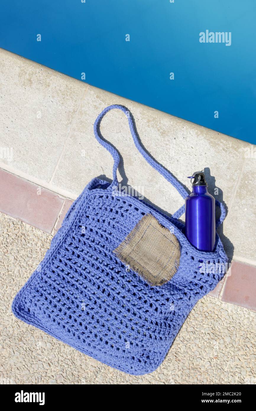 Blaue, leichte, wiederverwendbare Aluminiumflasche in handgemachter Tragetasche am Pool, nachhaltiger, abfallfreier Lebensstil Stockfoto
