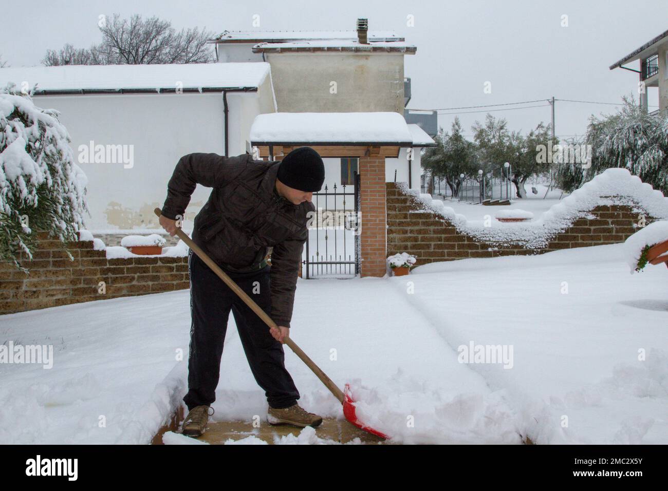 Bild eines Mannes mit einer Schaufel, der mühsam Schnee aus seiner Einfahrt schaufelt. Stockfoto