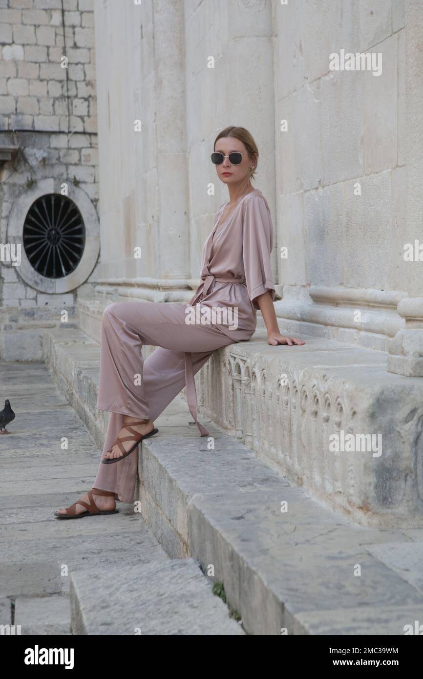 Modische Touristin in seidenbeigefarbenem einfarbigem Outfit in den Straßen der historischen Stadt Trogir, Kroatien Stockfoto