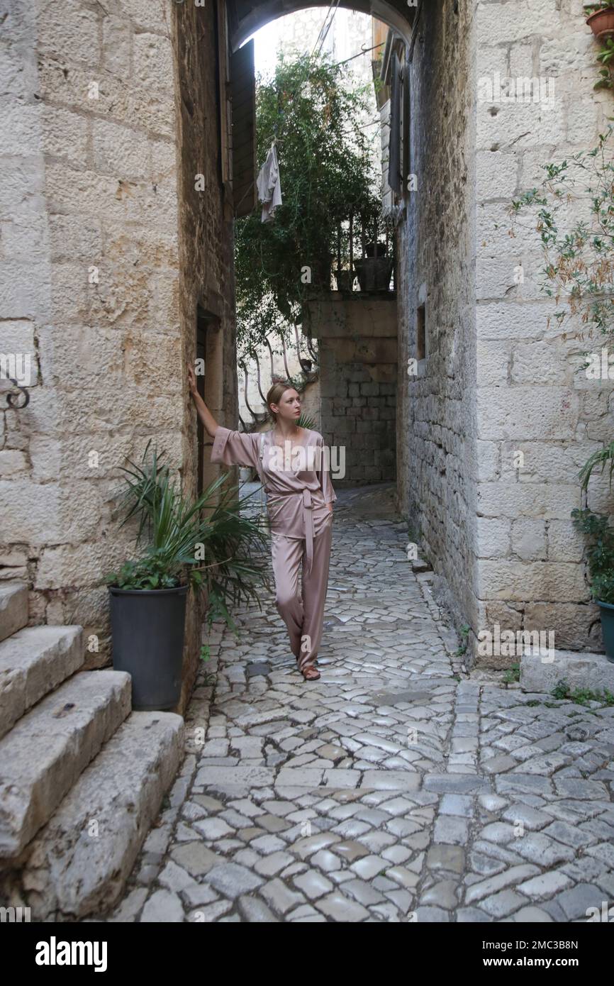 Modische Touristin in seidenbeigefarbenem einfarbigem Outfit in den Straßen der historischen Stadt Trogir, Kroatien Stockfoto