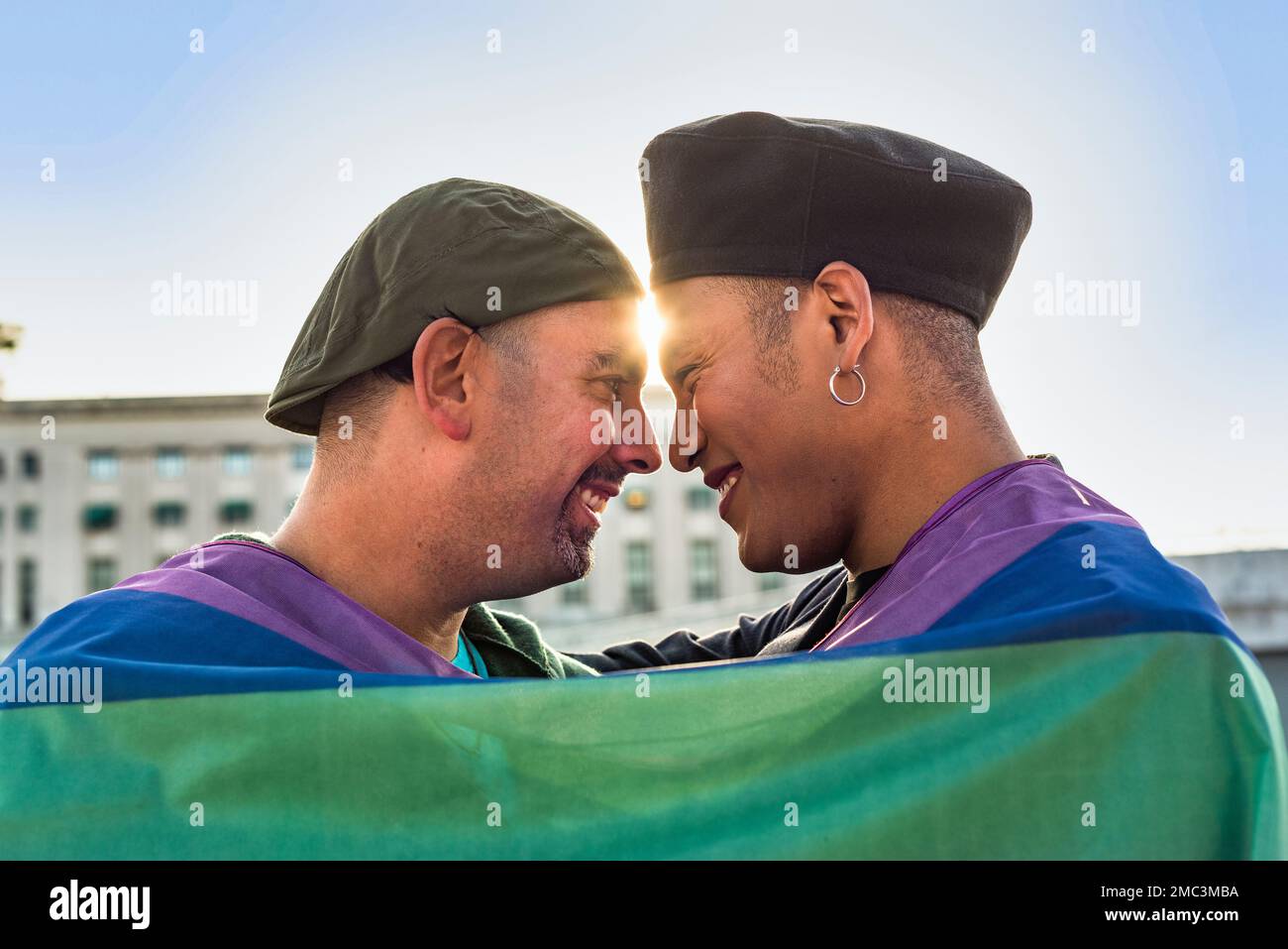 Schwules Paar unter der LGBT-Regenbogenflagge, während es lacht und sich ansieht. Konzept des Stolzes. Pride-Monat. Stockfoto