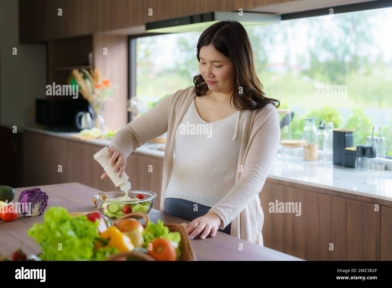 Schöne asiatische schwangere Frau bereitete gerne einen Gemüsesalat, Bio gesunde Lebensmittel, in einer gemütlichen Küche zu Hause zu. Stockfoto