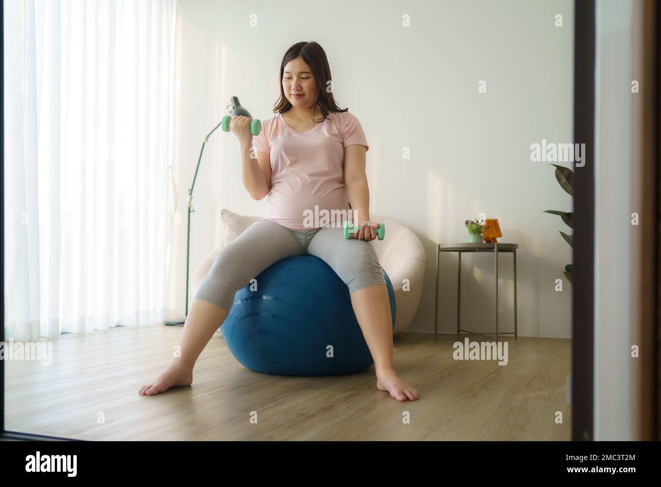 Schöne asiatische schwangere Frau, die zu Hause mit Kurzhanteln trainiert, gesundes Konzept Stockfoto