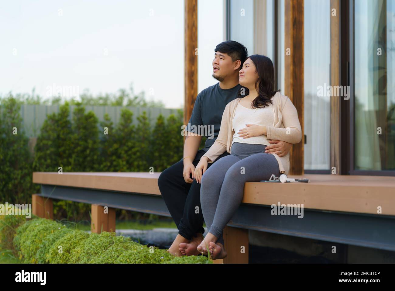 Schwangere Asiatin mit ihrem Mann, die sich zu Hause auf der Terrasse unterhalten, um zu entspannen und frische Luft zu atmen. Stockfoto