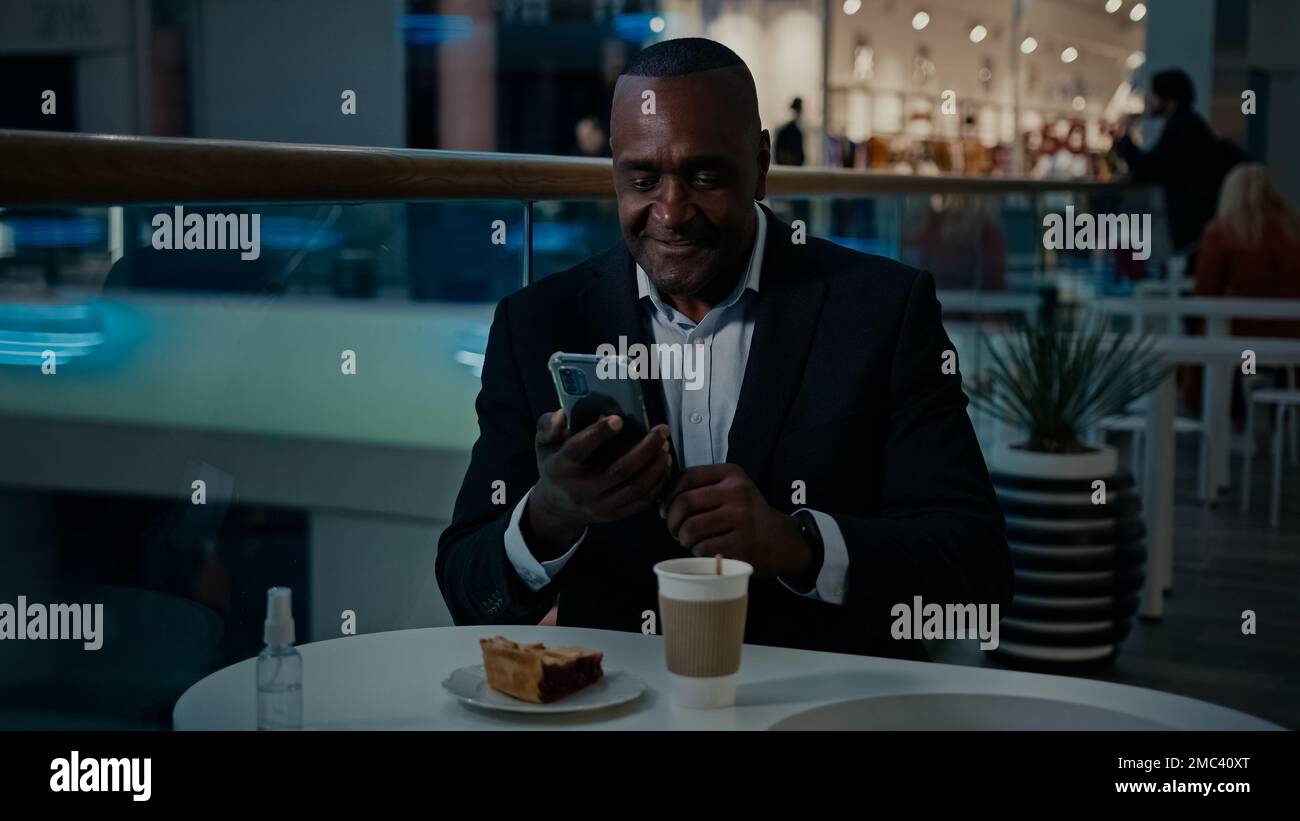 Reifer erwachsener, afroamerikanischer Geschäftsmann mittleren Alters, der im Café mit Kaffee, Tee und einem Stück Kuchen sitzt, macht ein Foto-Selfie mit dem Handy Stockfoto