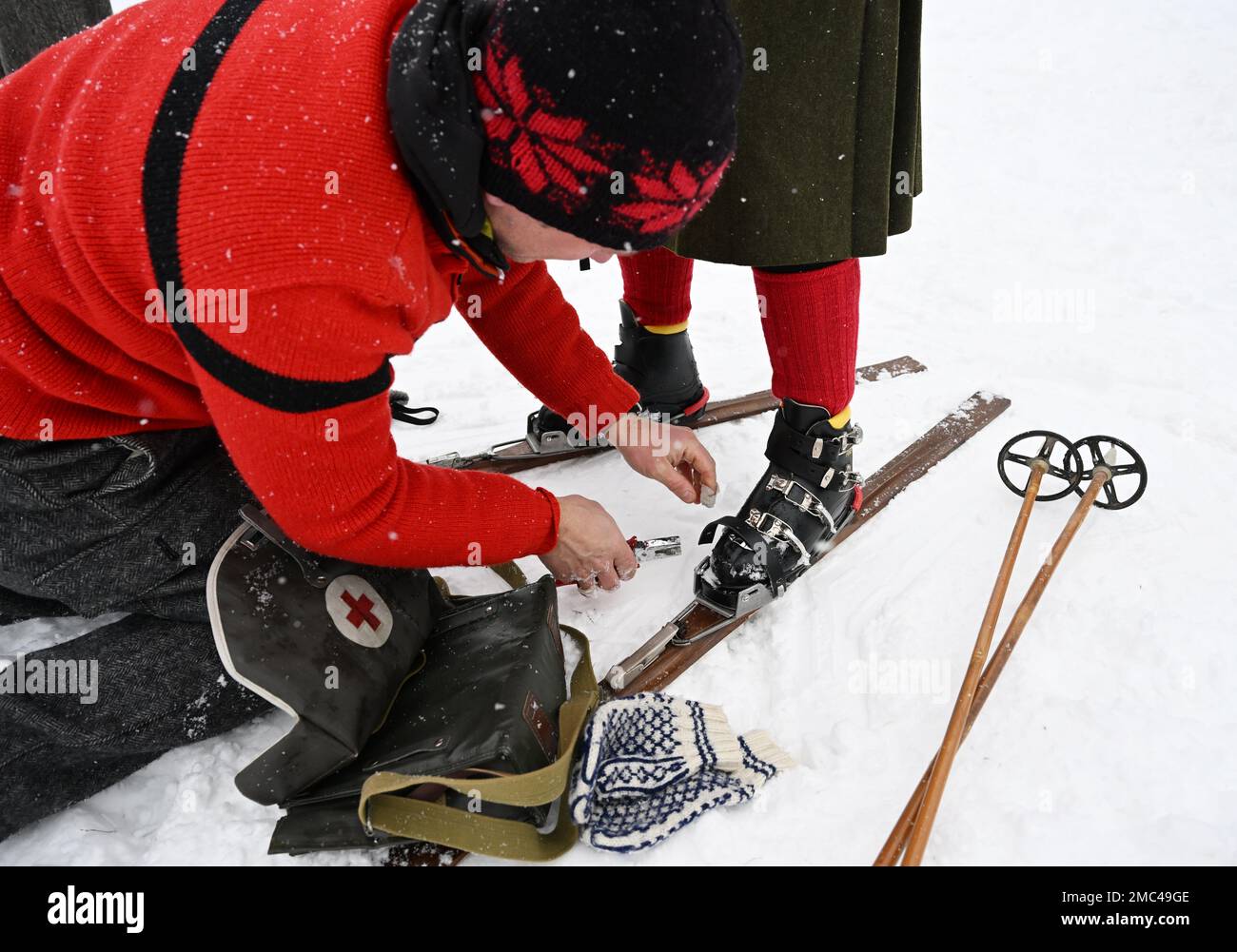 Bayern, Deutschland. 21. Januar 2023. 21. Januar 2023, Bayern, Krün: Ein Teilnehmer passt die Bindung eines anderen Teilnehmers an Holzskiern vor dem „Nostalski“-Skirennen im Barmsee-Lift an. Mit alten Holzskiern und Schnürsenkel aus Leder, zumindest aus dem vergangenen Jahrhundert, starten die Teilnehmer ein lustiges Rennen. Foto: Angelika Warmuth/dpa Credit: dpa Picture Alliance/Alamy Live News Stockfoto