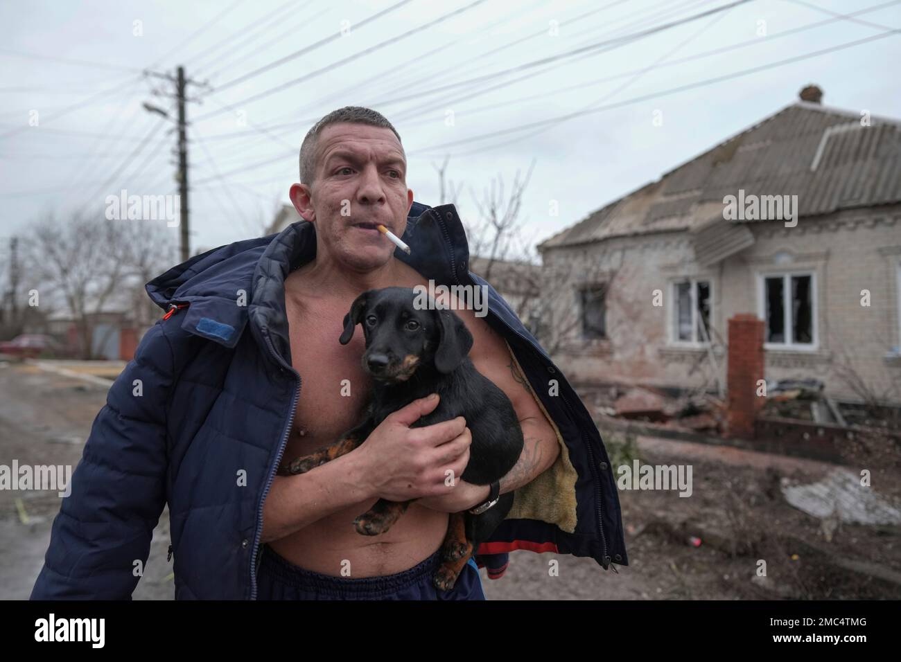 A man holds a dog as he walks past a damaged house following Russian shelling, in Mariupol, Ukraine, Thursday, Feb. 24, 2022. Russia launched a wide-ranging attack on Ukraine on Thursday, hitting cities and bases with airstrikes or shelling, as civilians piled into trains and cars to flee. (AP Photo/Evgeniy Maloletka) Stockfoto