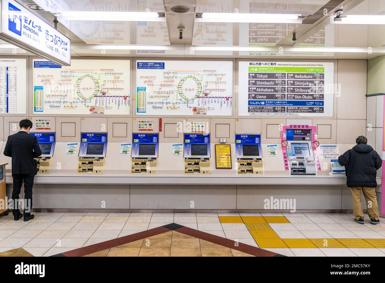 Tokio Haneda Airport. Interieur von Terminal 1. Reihe von Tokio Monorail Fahrkartenautomaten und zwei Menschen, die sie verwenden. Über Maschinen, Karten und Preise. Stockfoto