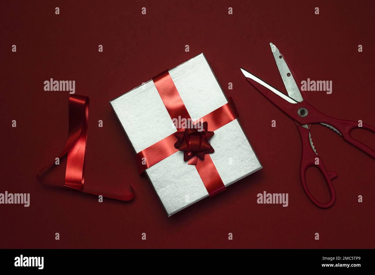 Geschenkbox mit rotem Band und Schere auf rotem Hintergrund, Draufsicht Stockfoto