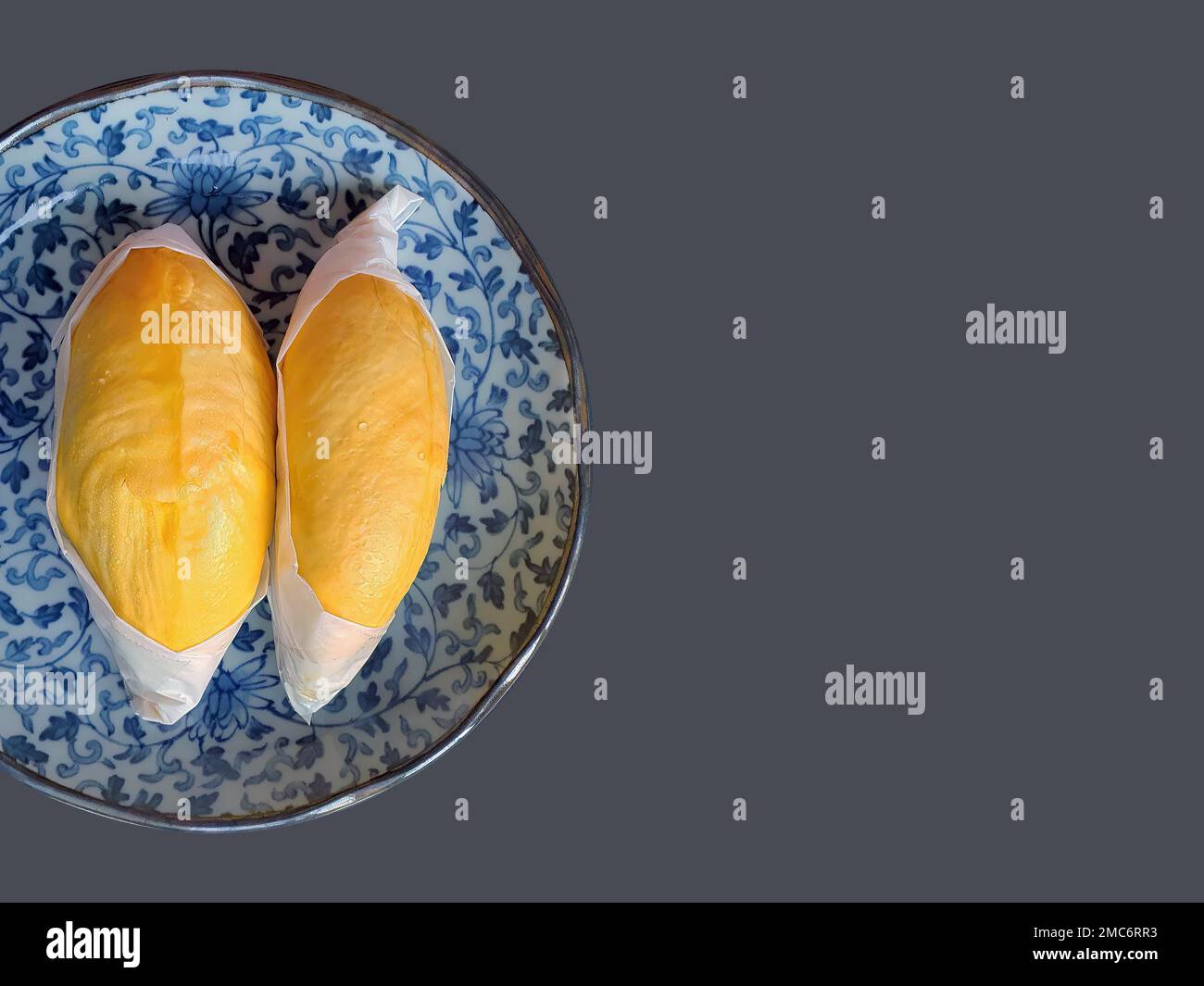 Zwei goldgelbe Fleischsorten von Durian, eingewickelt mit weißem Papier, König der Früchte, natürliche Form und Form, König der Früchte, grauer Hintergrund, isoliert, mit Stockfoto
