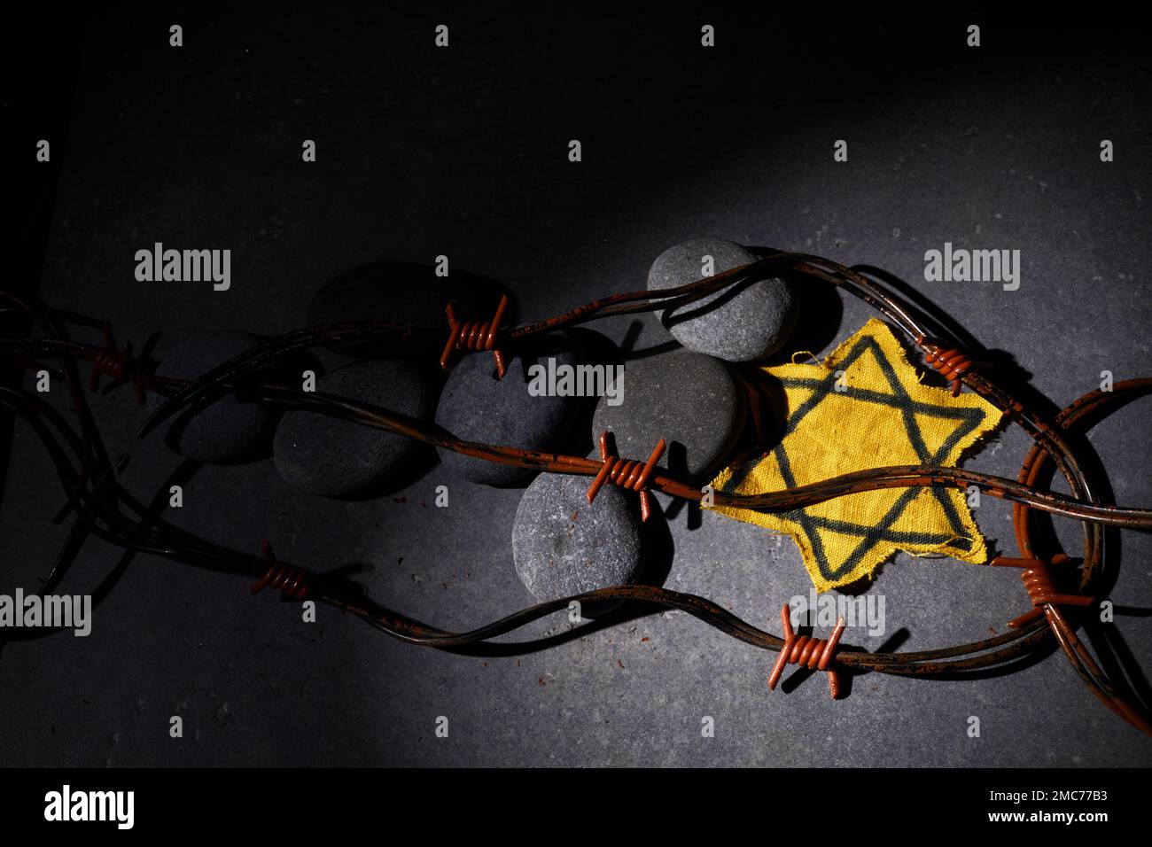 Holocaust-Gedächtnisfeiertag. Stacheldraht, Steine und gelber Stern auf dunklem Hintergrund Stockfoto