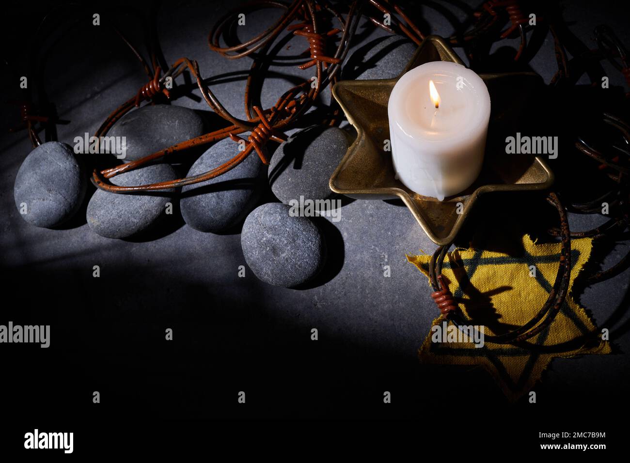 Holocaust-Gedächtnisfeiertag. Stacheldraht, Steine, gelber Stern und brennende Kerze auf schwarzem Hintergrund Stockfoto